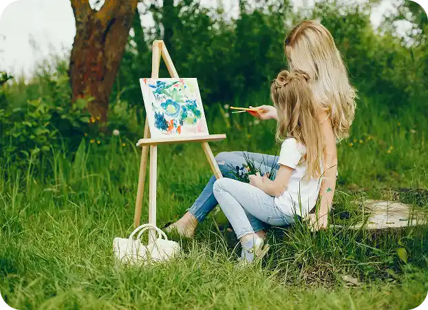 Mum and daughter are painting something abstract on a canvas on an easel, holding flowers.